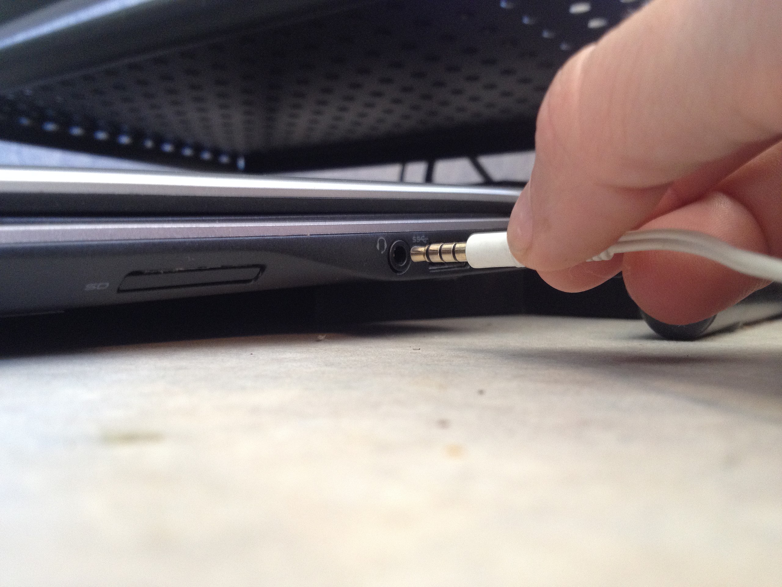 Person plugging in headphone jack into laptop audio port